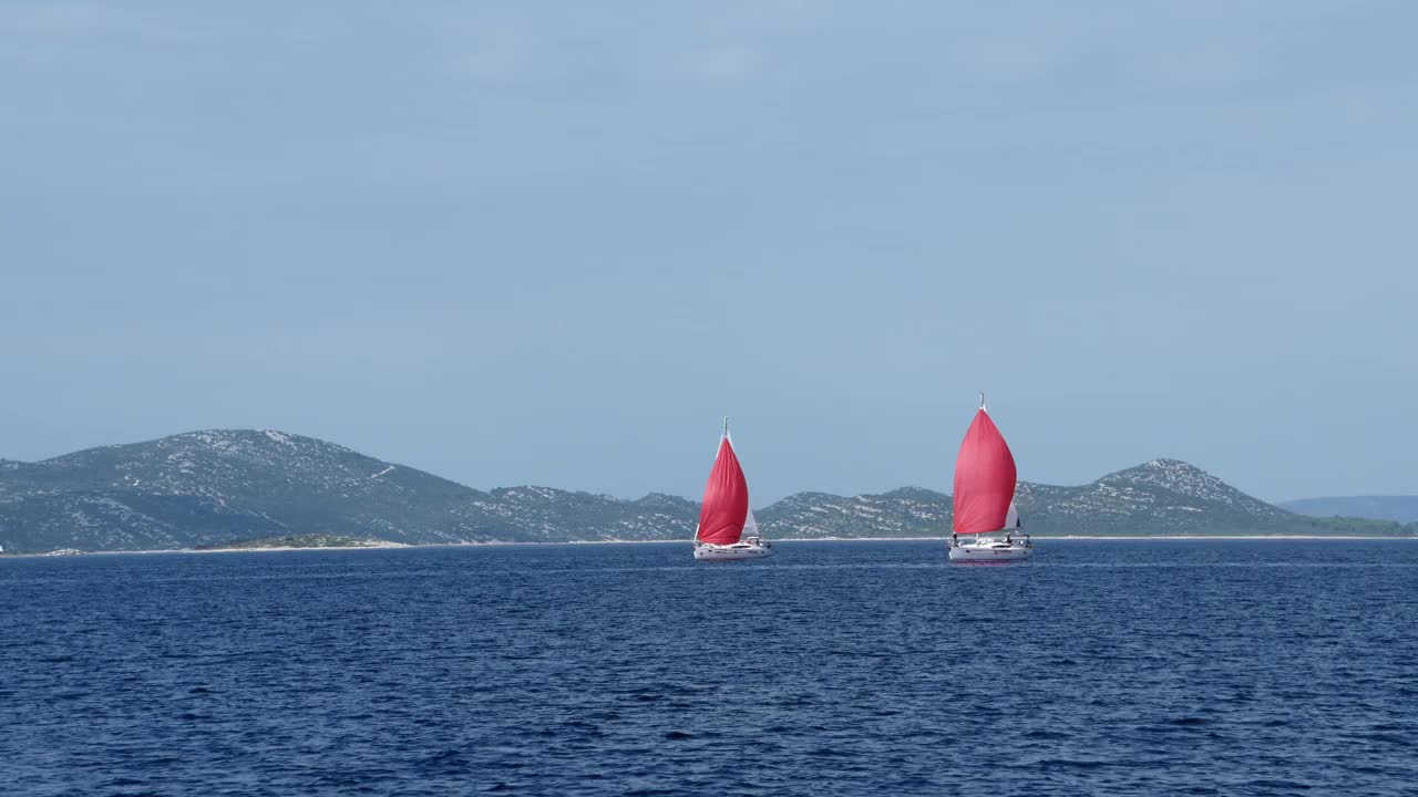 两艘帆船在海上航行，其中一艘是红色的视频素材