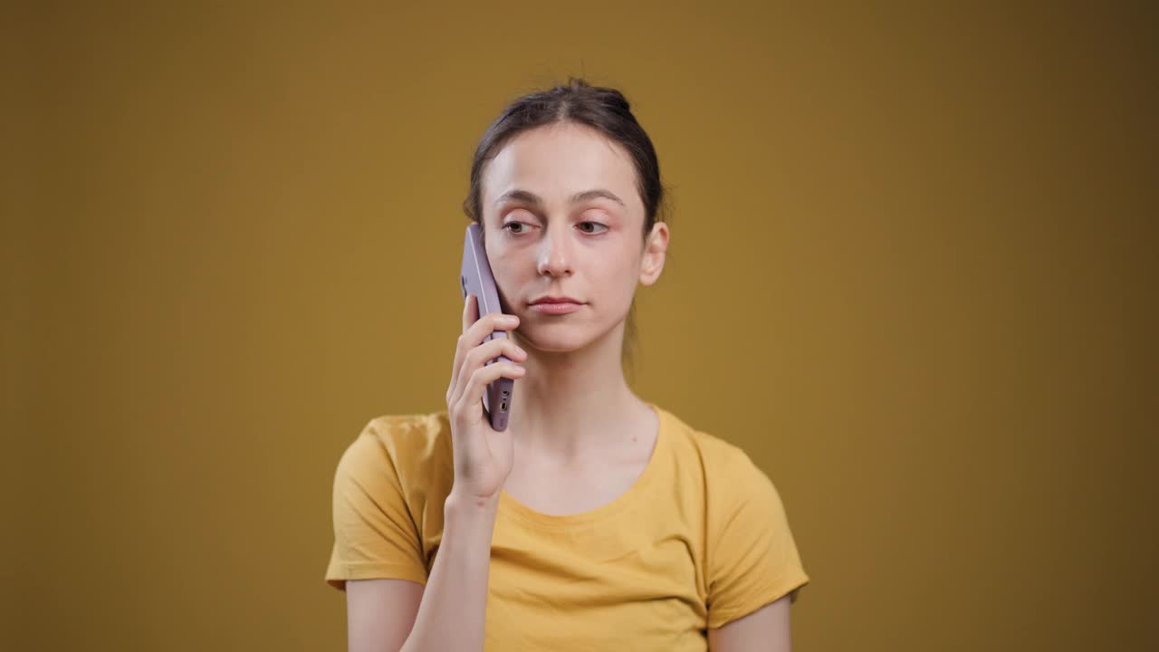 一名身着休闲装的年轻女性正在接听电话，在赭色背景下，她的表情十分专注。视频素材