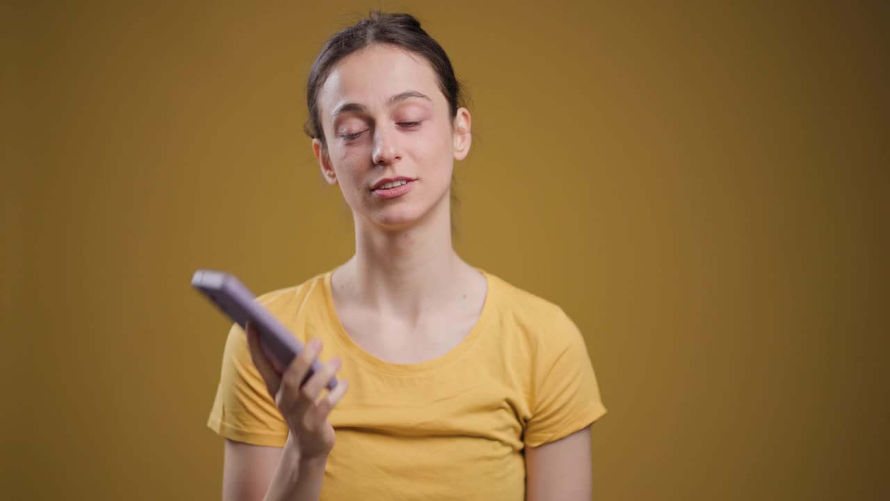 一名年轻女子站在纯黄色背景下讲电话，显得紧张而焦虑。视频素材