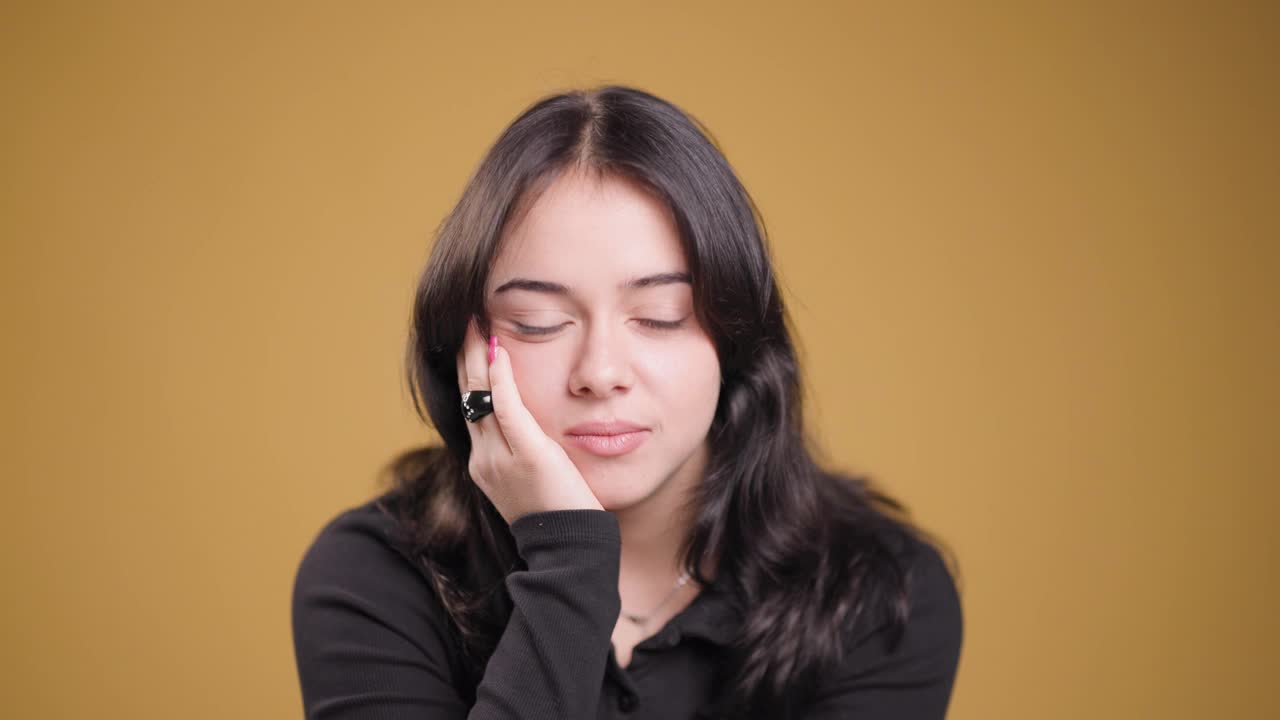 穿着黑色衬衫，黄色背景上有一双富有表情的眼睛的体贴的年轻女子视频素材