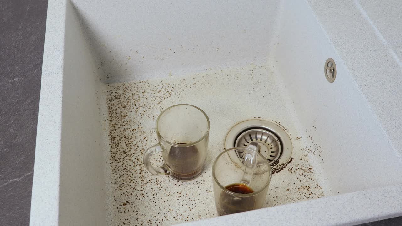 一个女人正在洗一个脏杯子。洗脸盆水槽的排水堵塞。被咖啡弄脏的水槽。近景。视频下载