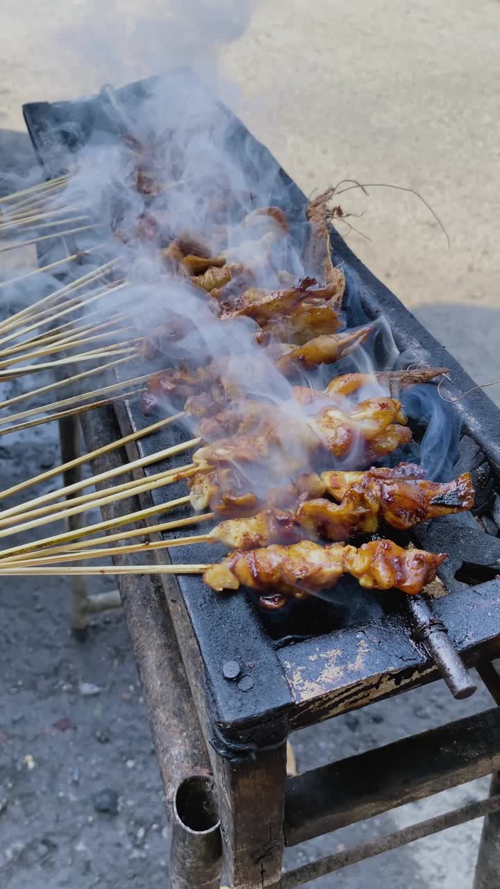 街头小吃摊贩烤沙爹，烤肉串。烤肉架上的肉是印尼产的沙茶。视频下载