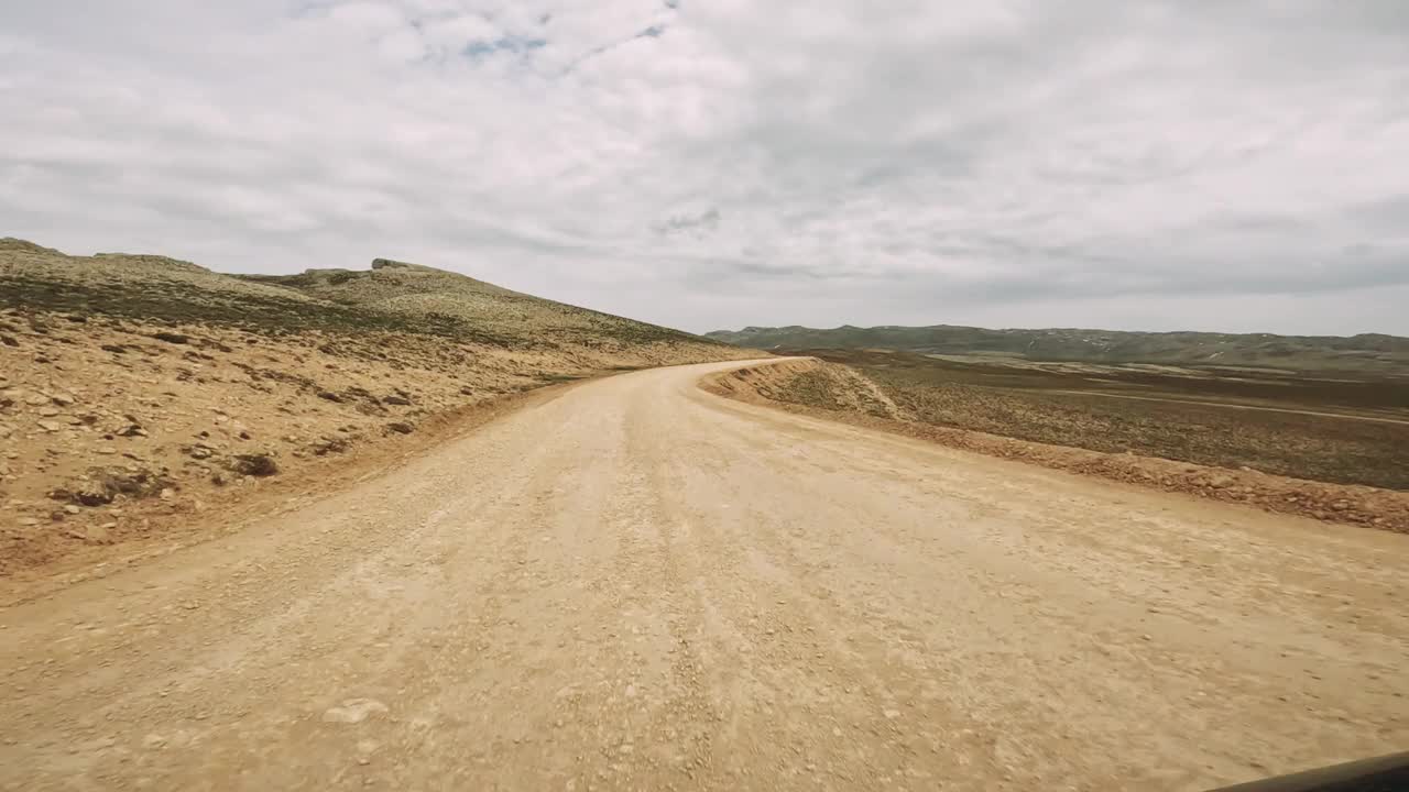 一辆汽车优雅地蜿蜒在尘土飞扬的沙漠道路上，周围是广阔的沙质景观和高耸的山脉，展示了干旱荒野的雄伟之美视频素材