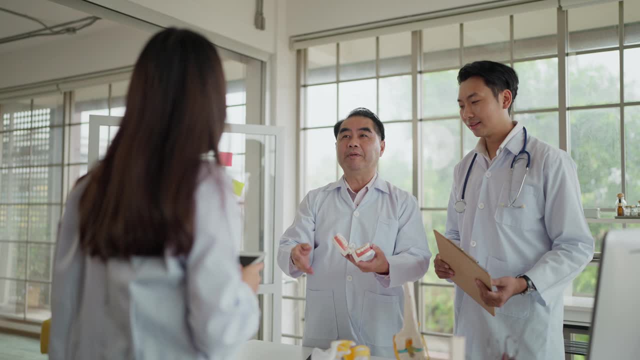 亚洲中年牙医讲师手持牙齿模型，在课堂上向一群学生牙医讲解人类牙齿的结构。牙医讲解口腔修复模型视频下载