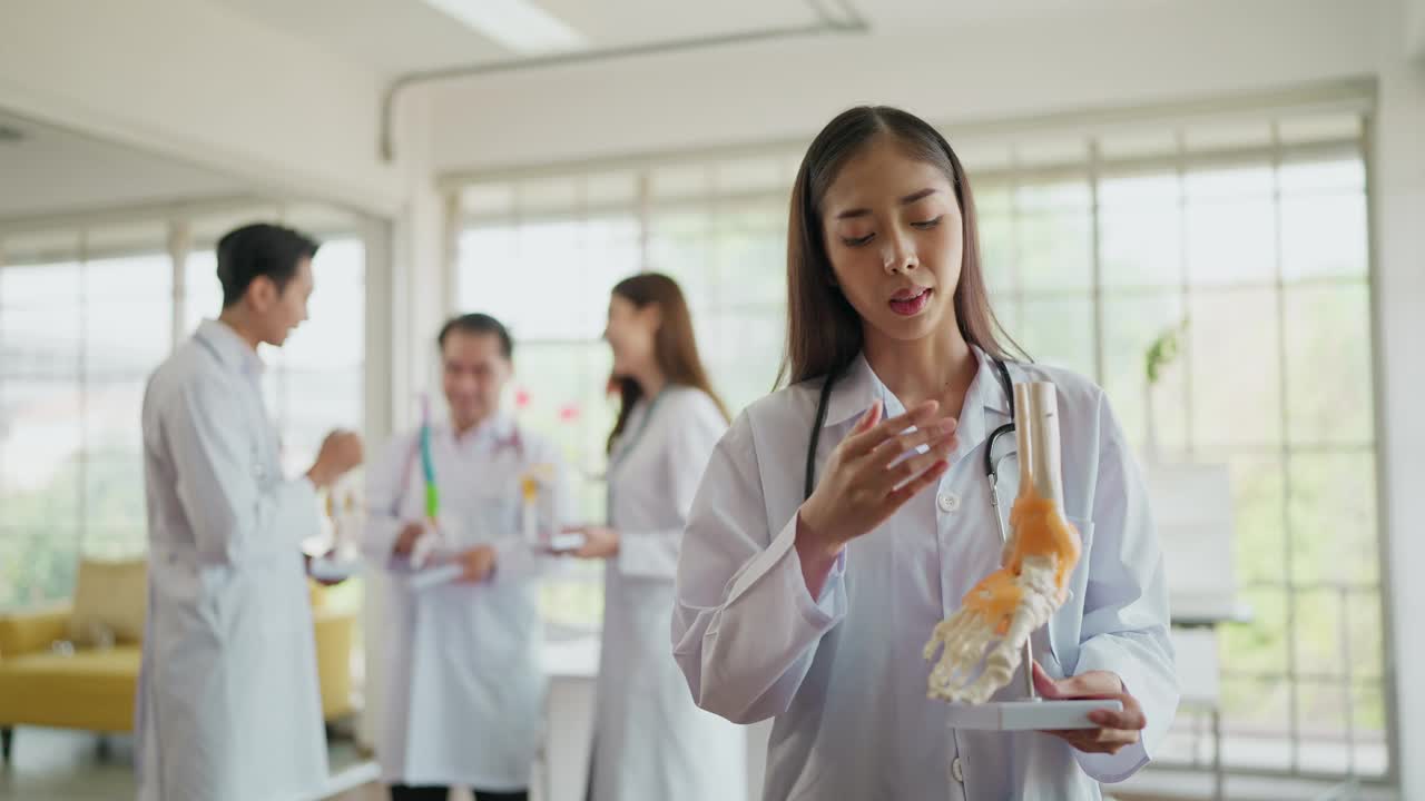 穿着制服的年轻亚洲女骨科医生手持人体踝骨骨架模型，同时通过在线视频向患者解释。医疗与科技视频下载