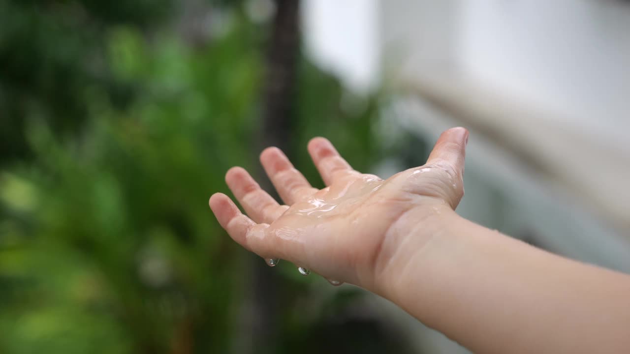 特写:孩子们的手在绿色植物的背景下抓着大雨滴。雨滴落在小手掌上，在阳光下闪闪发光。水晶雨滴，大自然的小奇迹，给孩子们带来快乐。视频下载