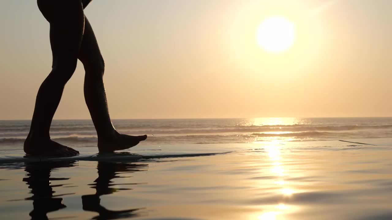 海边五颜六色的夕阳，岸边孩子们的脚的剪影轻轻地踏在水面上。无忧无虑的孩子们在落日的余晖中沿着海边散步。海浪洗孩子的脚。宁静安逸的童年视频下载