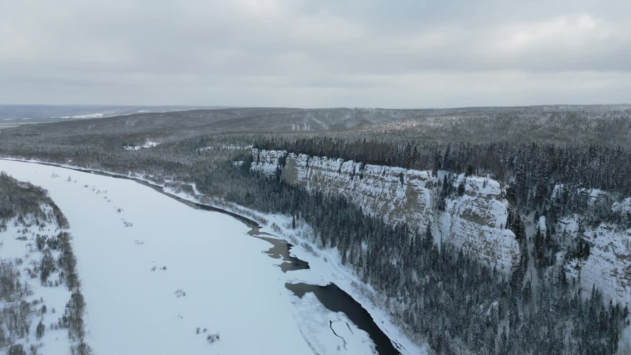 冬季森林景观和松树林生长在悬崖上的冻结的河流在雪。夹。令人叹为观止的鸟瞰自然景观。视频素材