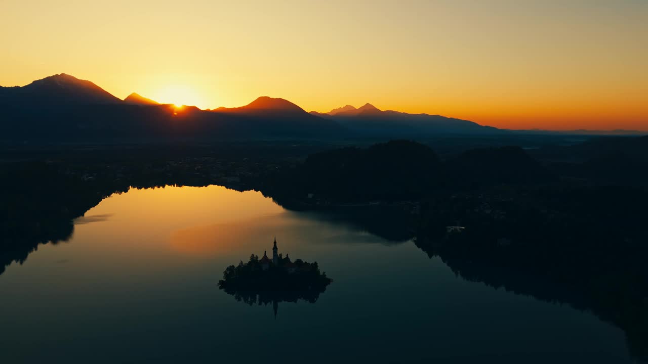 空中无人机拍摄的剪影小岛在平静的湖在日落时对阿尔卑斯山流血视频素材