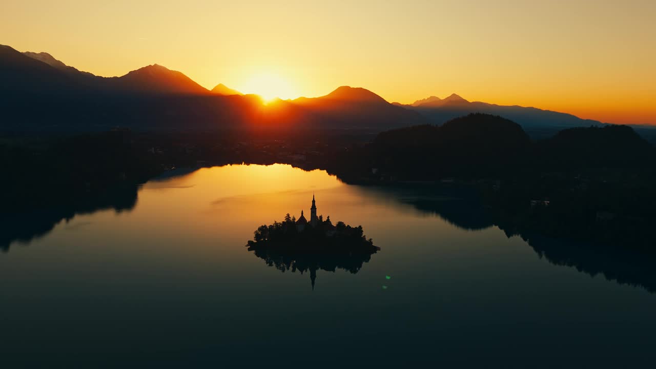 空中无人机拍摄的剪影教堂在湖中央的小岛上对山日落视频素材