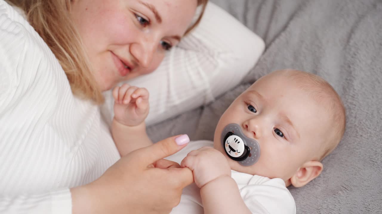 刚出生的孩子带着乳头躺在妈妈的床上，妈妈抱着孩子，婴儿感到安全。母性、童年、育儿、产假的概念视频素材