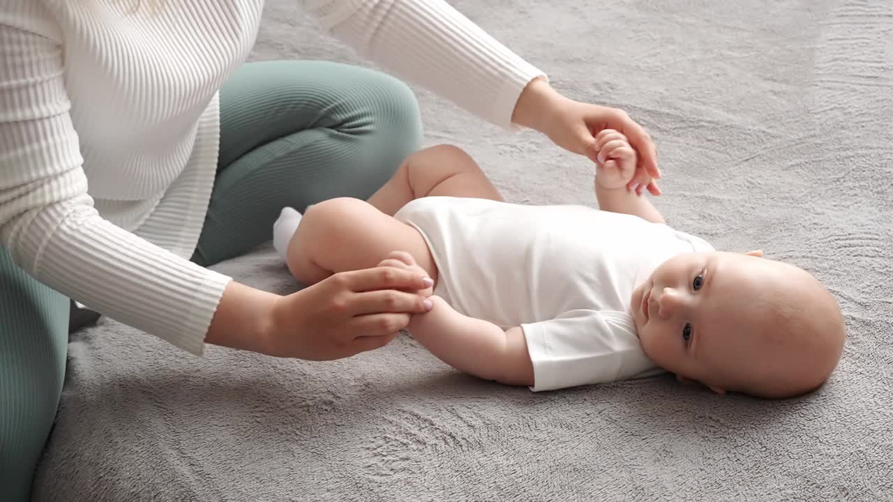 妈妈为快乐的宝宝做体操。妇女对着躺在床上的婴儿做早操，手臂时而弯曲时而舒展。小儿保健，小儿推拿，预防小儿肥厚。视频素材