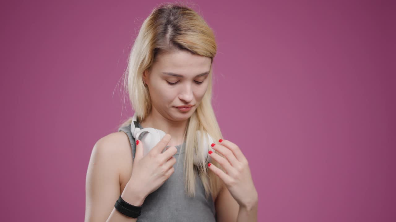 年轻的金发女子通过白色耳机在粉红色的背景下欣赏音乐视频素材