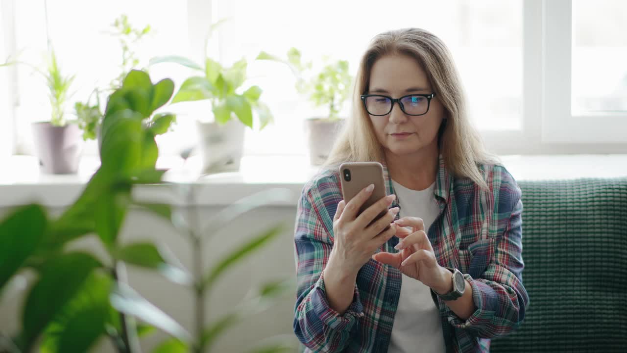 一位放松的中年妇女坐在沙发上玩手机视频素材