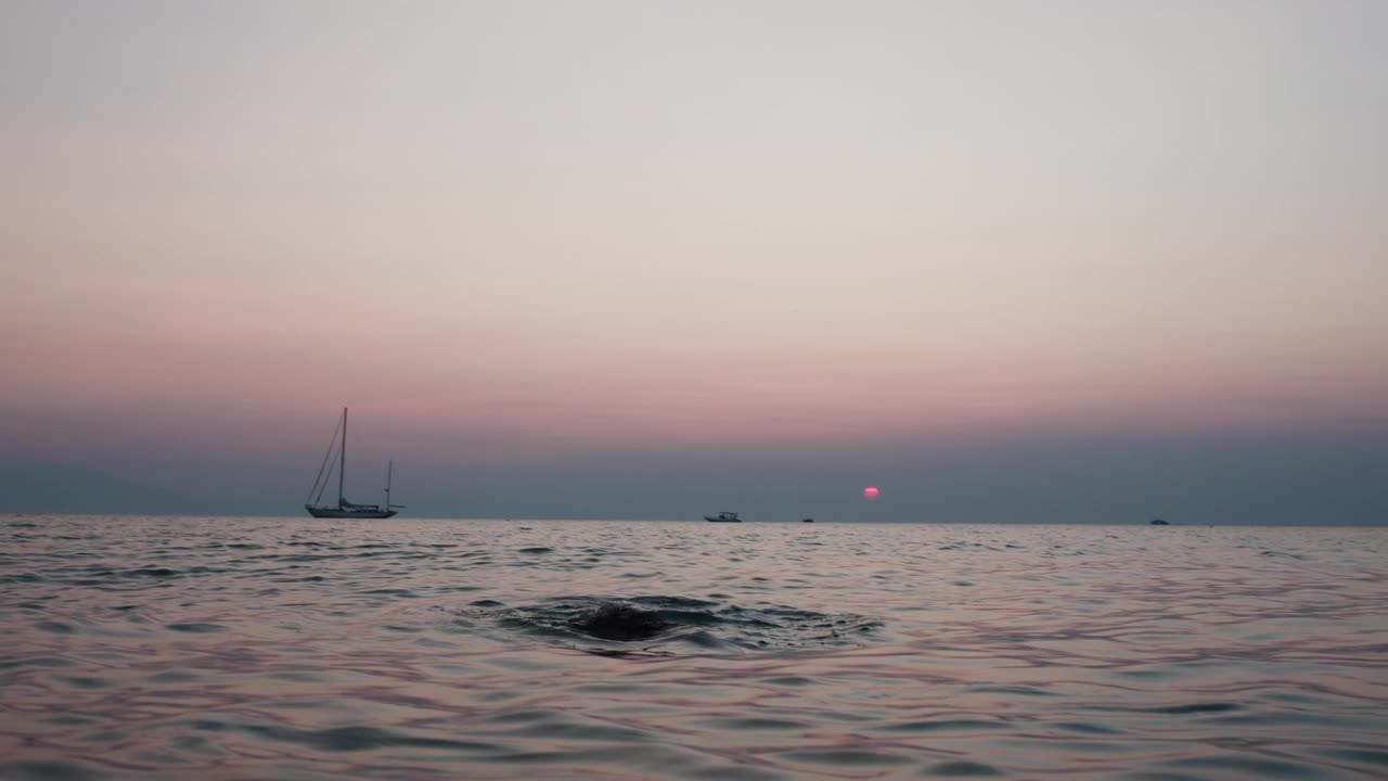 男子在日落时分跑进大海，在宁静的海滩背景下溅起水花视频素材