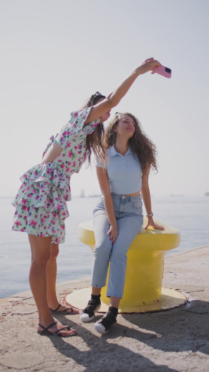 两个年轻女子在一个阳光明媚的日子里在海边码头自拍视频素材