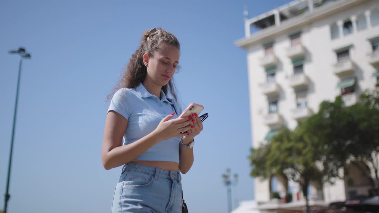 年轻女子在城市环境中使用智能手机，背景是阳光明媚的拱廊和建筑视频素材