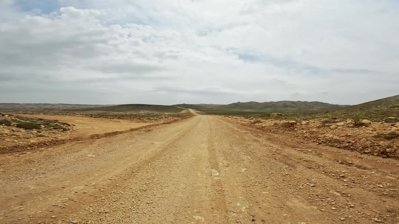 沿着蜿蜒的土路踏上一段迷人的旅程，穿过沙漠的中心，提供令人叹为观止的干旱景观视频素材