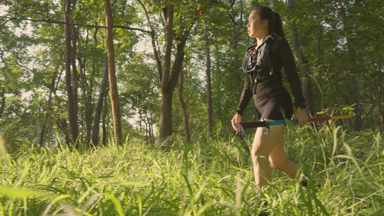 一个女人正穿过森林，手里拿着一根绿蓝相间的杆子视频下载