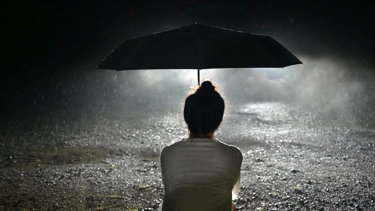 女人撑着伞独自走在下雨天的路上。慢镜头。视频下载