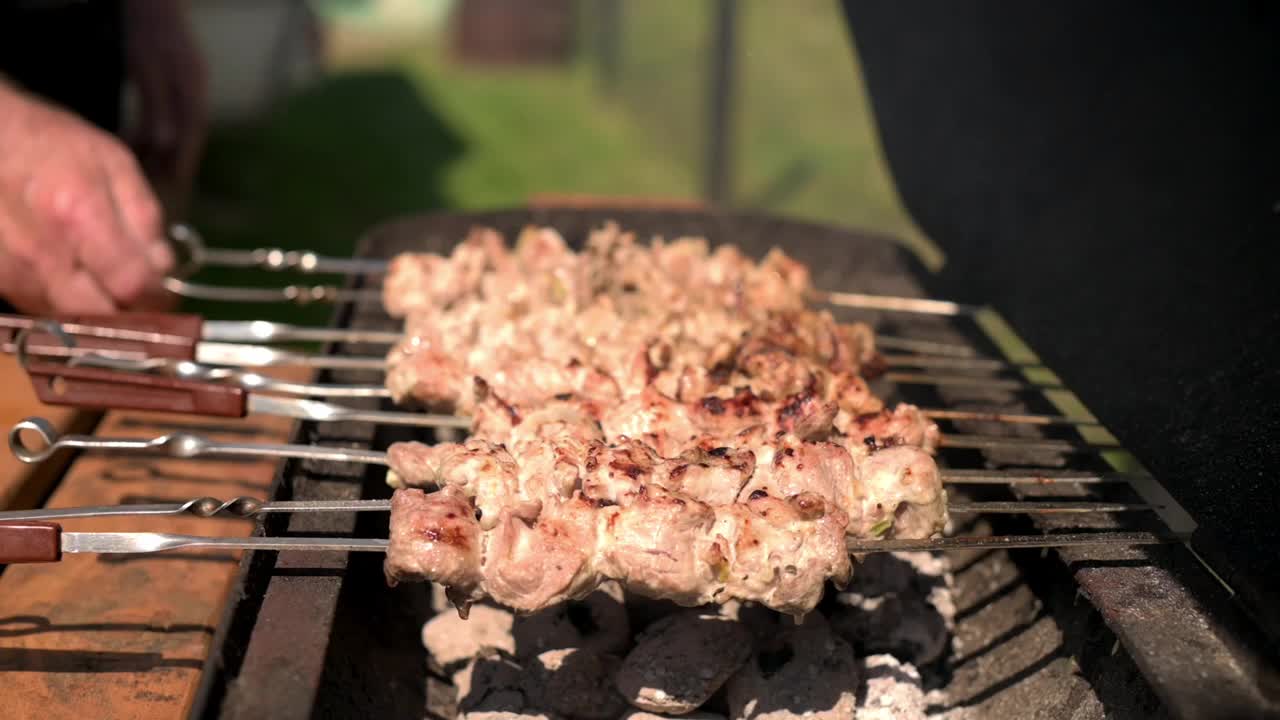 在阳光明媚的日子里烧烤串肉，熟练的手转动串增加了动态的人文元素，强调了在每一块上实现完美烧烤痕迹所涉及的关怀和技术视频素材