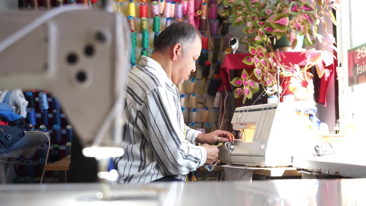 拉丁裔男子在他的服装店用缝纫机缝纫视频素材