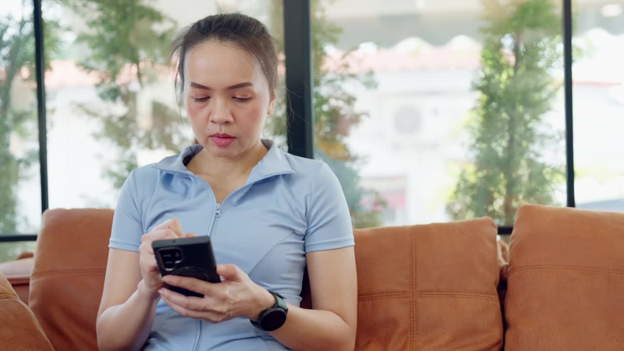 一个女人坐在沙发上看她的手机视频下载