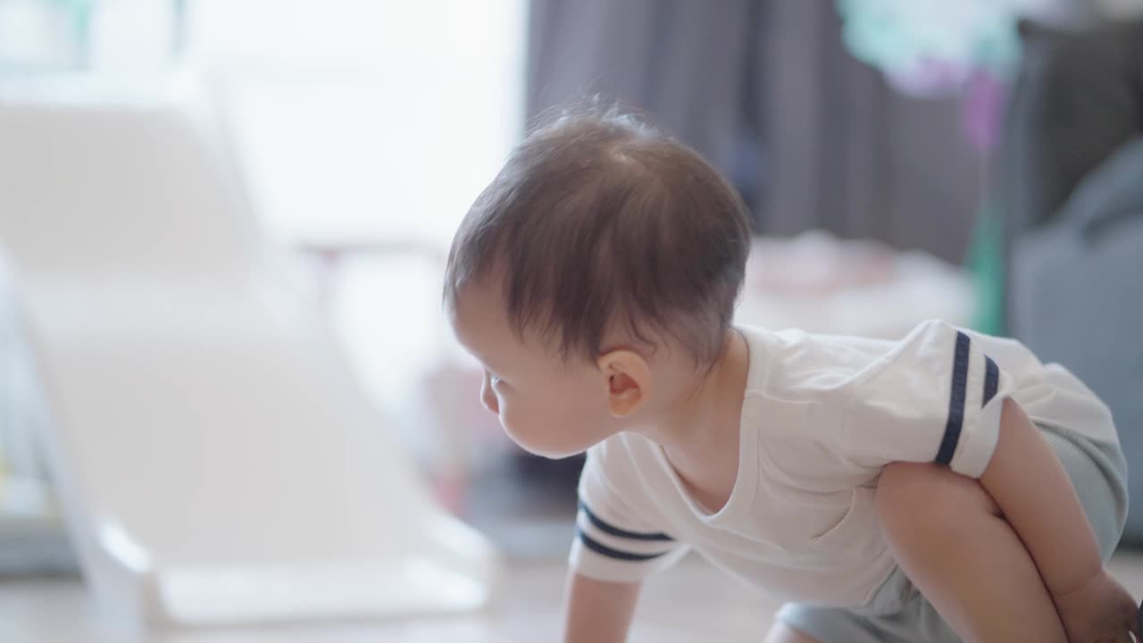 快乐的亚洲宝宝在房间里爬来爬去。蹒跚学步的男孩独自在房子里玩耍，学习如何爬行。视频素材