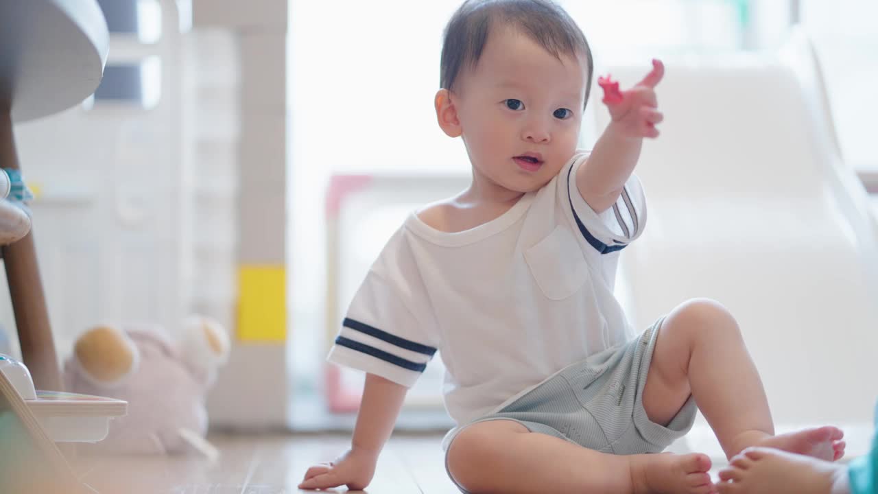 可爱的两岁亚洲幼童坐在客厅地板上玩五颜六色的干粘土，与天真的新生儿建立家庭纽带。视频素材