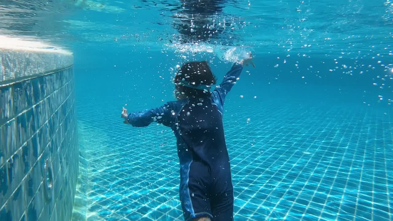 可爱的小男孩游进泳池，水面洒满阳光视频下载