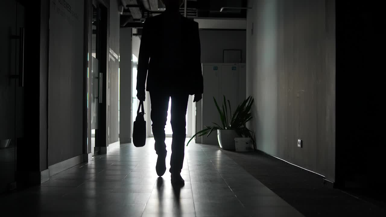 一个穿着正装的商人的腿的剪影沿着办公楼的走廊走着。视频素材