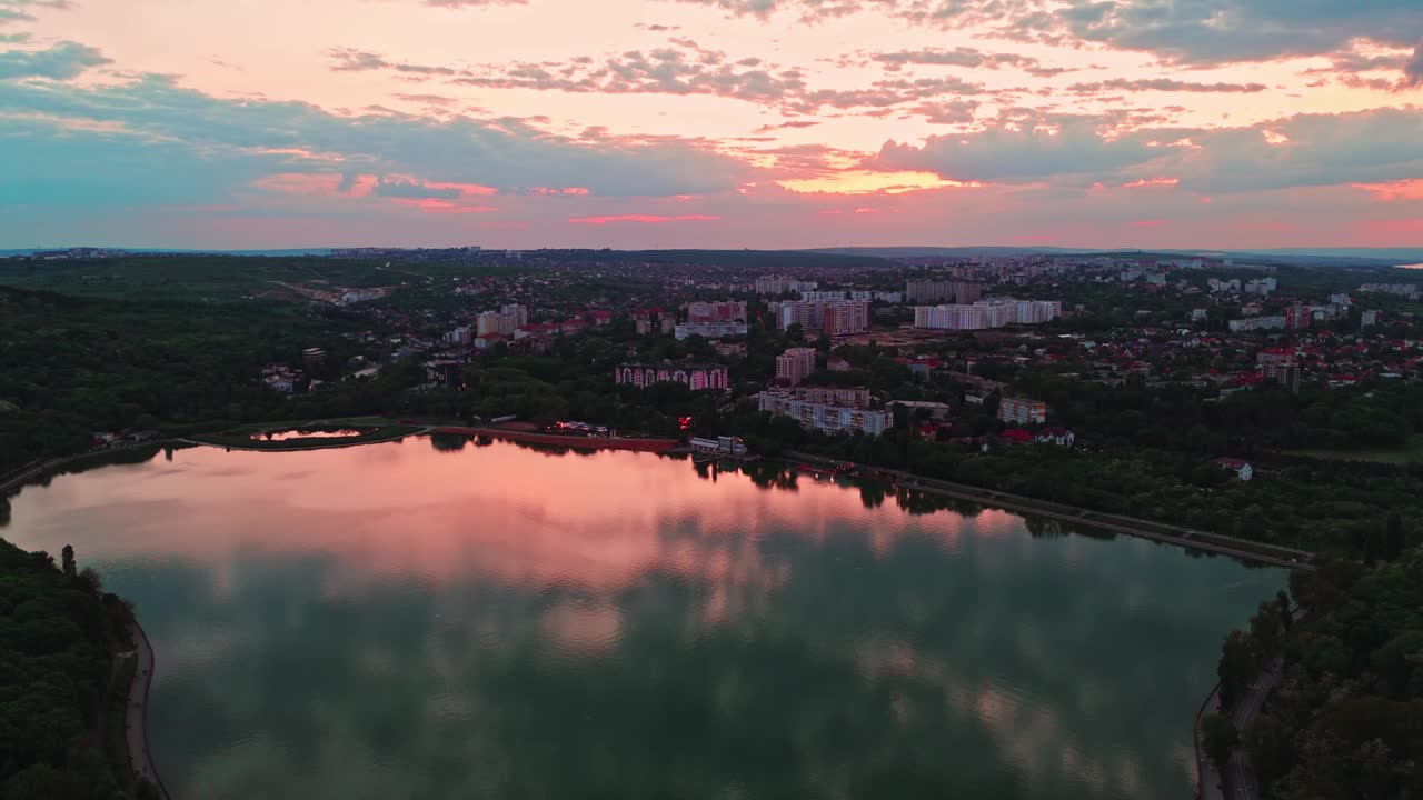 一个令人惊叹的日落鸟瞰一个宁静的湖对一个广阔的城市景观的背景。视频素材