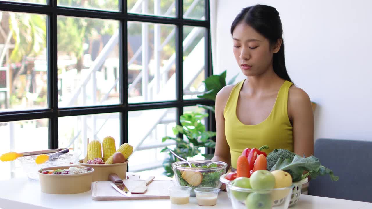 一位每天吃蔬菜沙拉的年轻亚洲女性对蔬菜感到厌倦。不快乐的女人在节食的时候看着叉子上的蔬菜。女孩不想吃蔬菜，不喜欢味道。视频素材