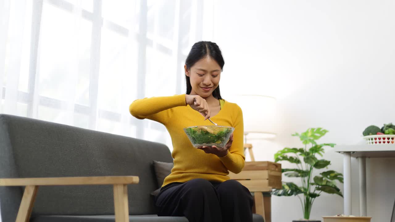 美丽健康的亚洲女人愉快地在家里吃美味的蔬菜沙拉。视频素材