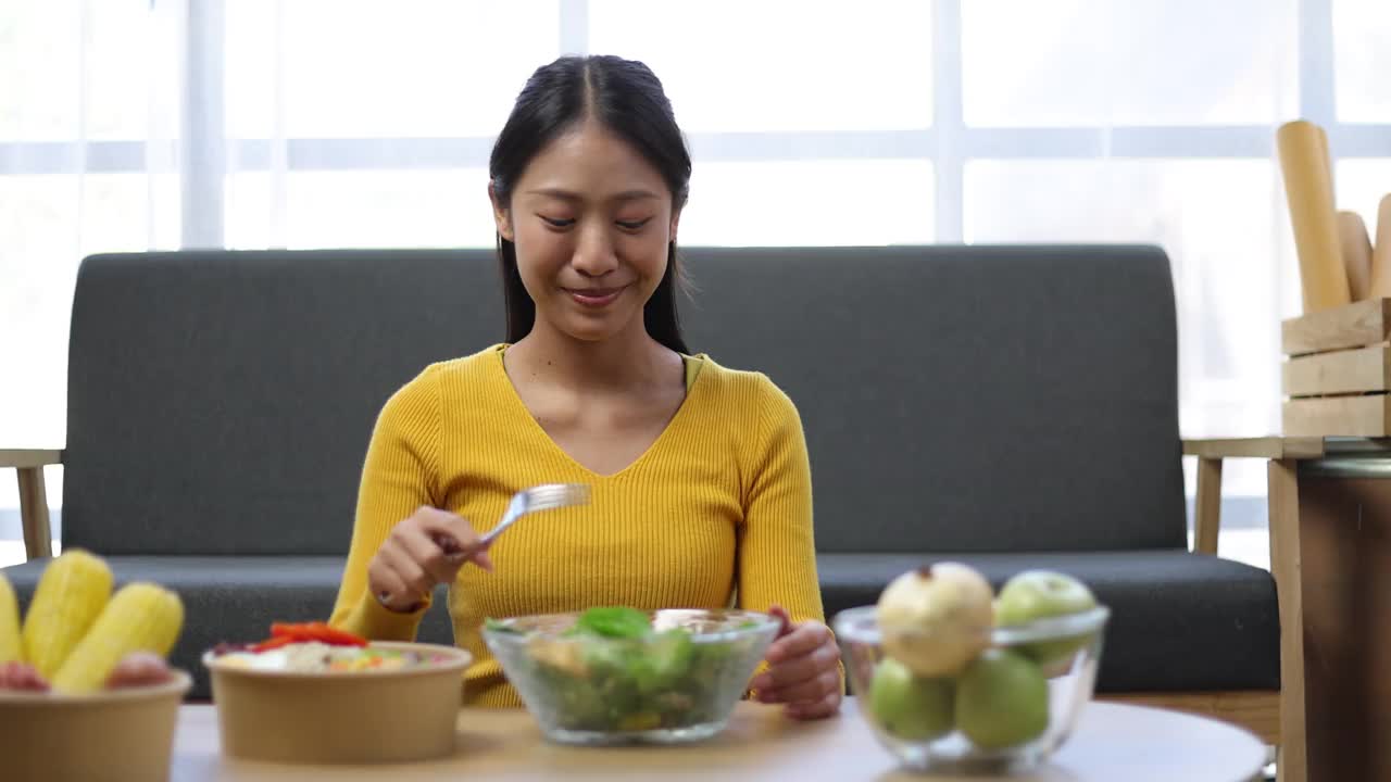 美丽健康的亚洲女人愉快地在家里吃美味的蔬菜沙拉。视频素材