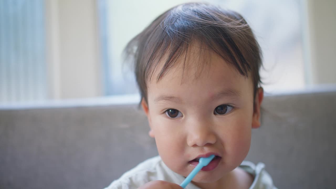 一个亚洲小孩正在用一把蓝色的牙刷刷牙。孩子在微笑，她很享受这个活动视频素材