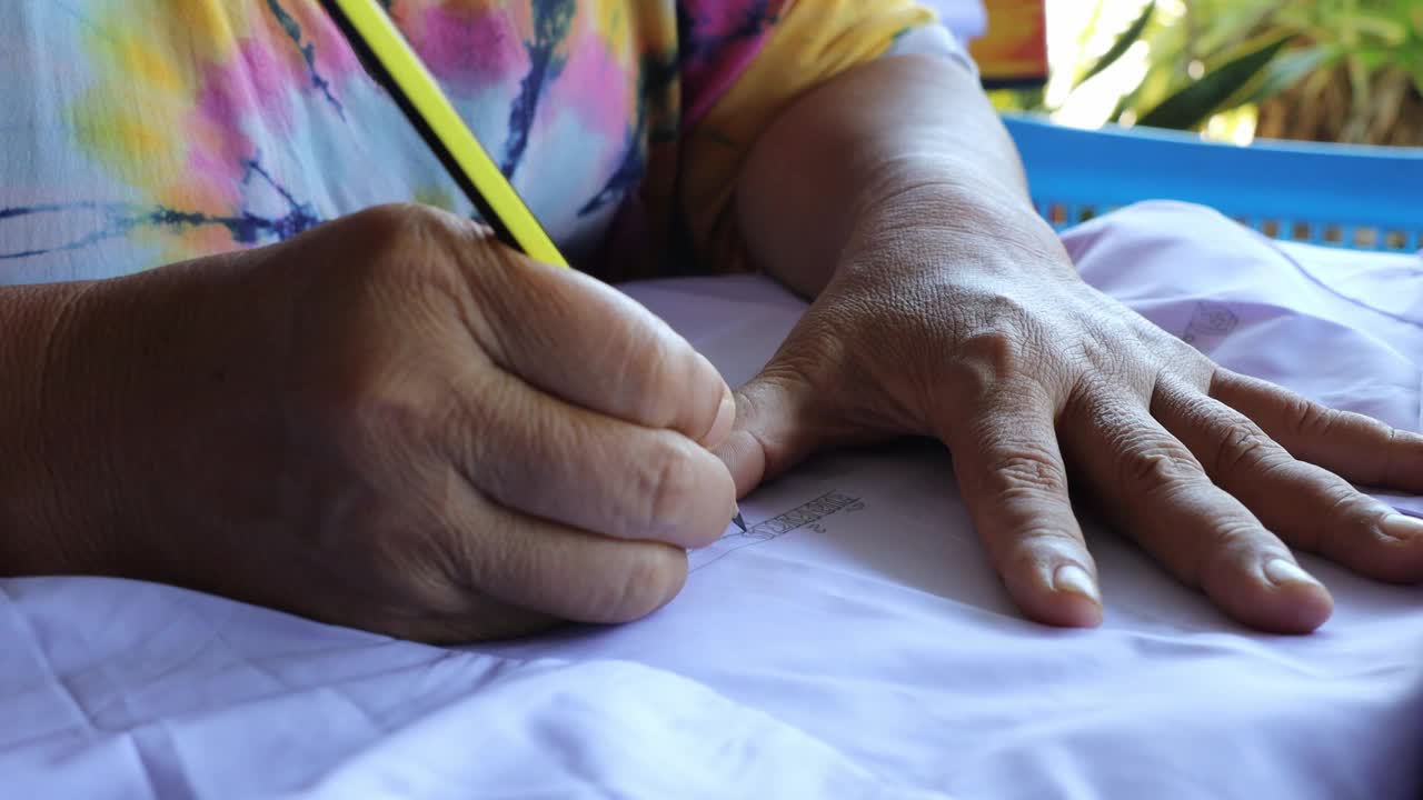 特写低角度观察一位泰国老妇人熟练地用手书写的书法图案。视频下载