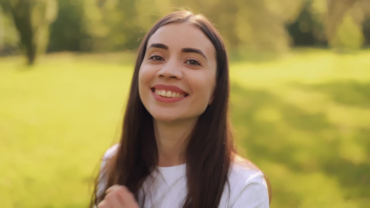 特写的年轻美丽可爱的微笑长发女子，女孩，女士户外绿色自然公园的背景视频下载