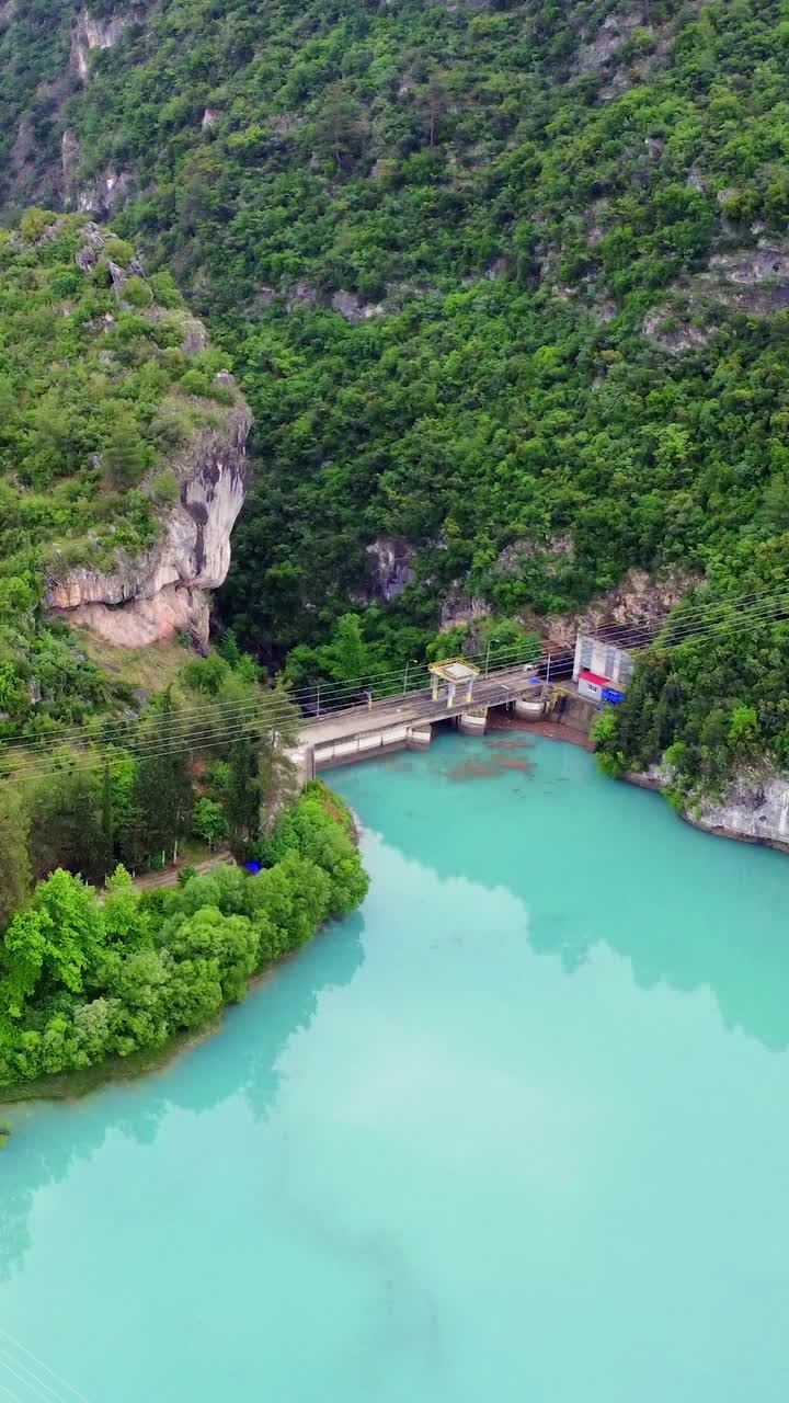 无人机看到的山绿松石湖和大坝。大坝横跨湖泊，突出水资源管理。绿松石湖映衬着周围的景观。大坝与湖泊的相互作用是显而易见的视频素材