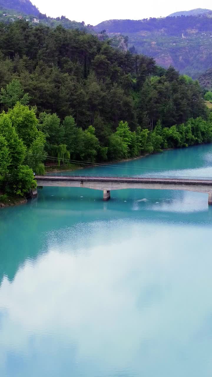 体验令人惊叹的空中镜头，一条绿松石河蜿蜒穿过山谷。飞越一个宁静的水库和翡翠山湖，设置在雄伟的高山。视频素材