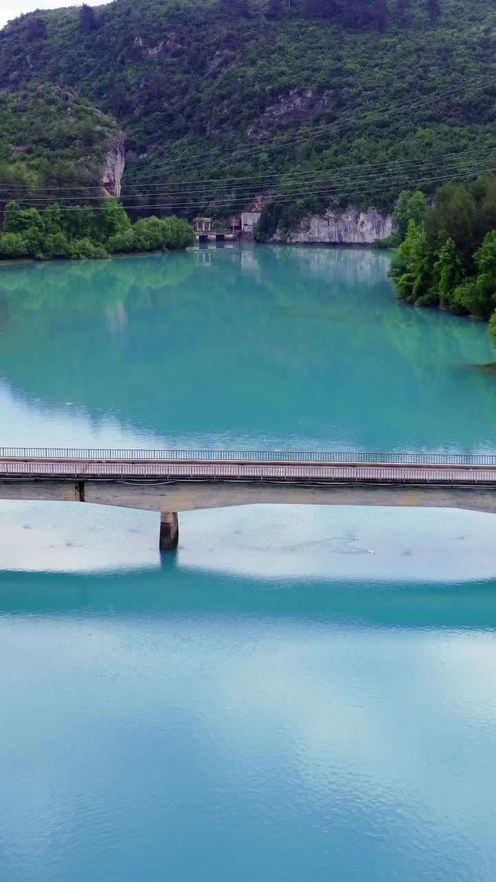 无人机捕捉山间湖上的桥梁，宁静的自然景色，桥梁连接海岸，建筑与自然无缝融合，宁静的山脉背景增强了桥梁景观视频素材