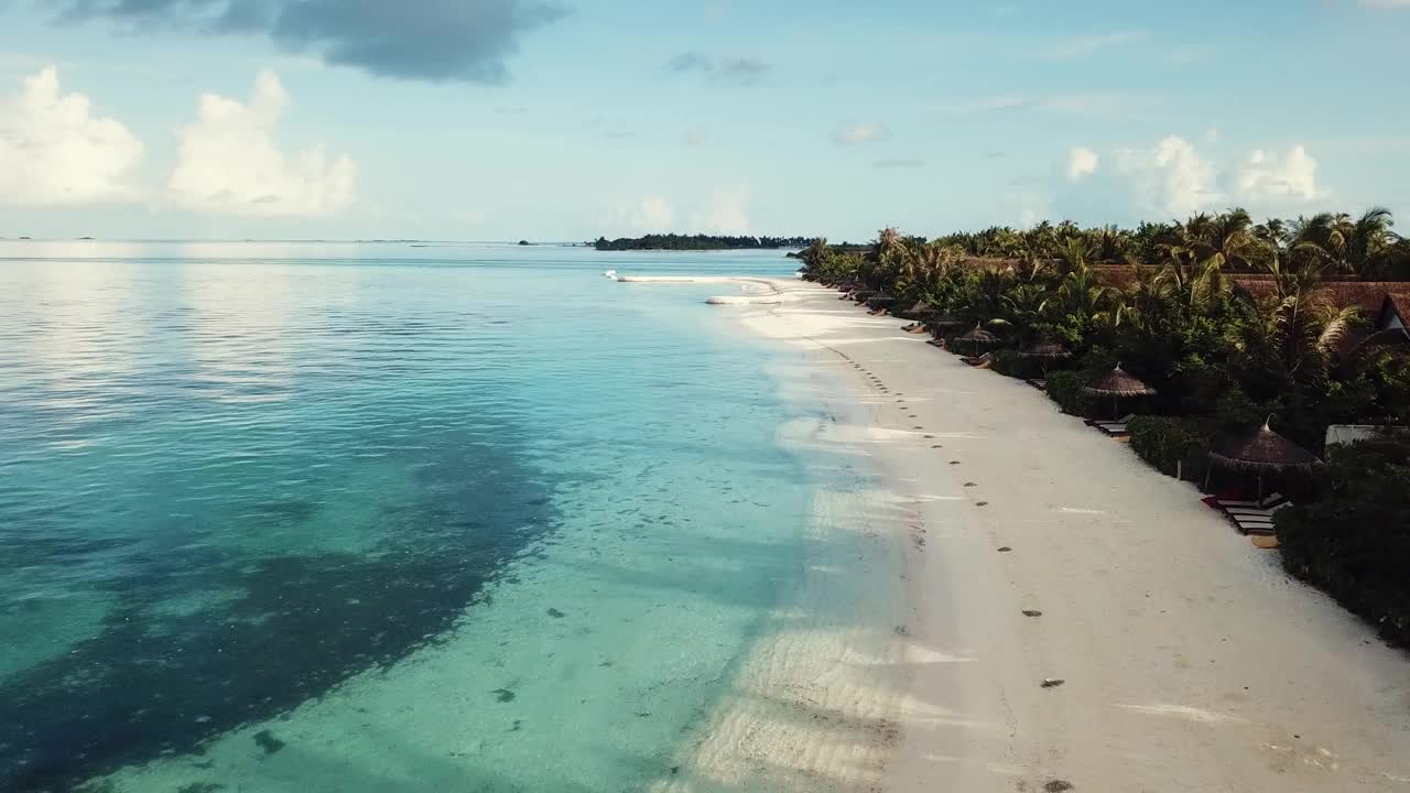 马尔代夫热带度假胜地的无人机视频，低空飞行，蓝色泻湖，绿色棕榈树，阳光明媚的天气，绿松石般的浅水，彩色日光浴床，4K视频素材