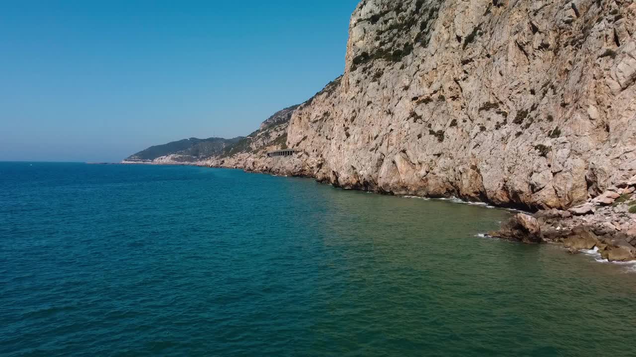 明亮的阳光下岩石丛生的海岸，展示着地中海水域的宁静，鸟瞰视频素材