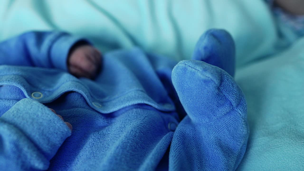 刚出生的婴儿安静地睡在蓝色的毯子上，捕捉着早期的宁静和天真。婴儿穿着柔软的蓝色衣服，闭着眼睛休息，周围是平静的气氛视频素材