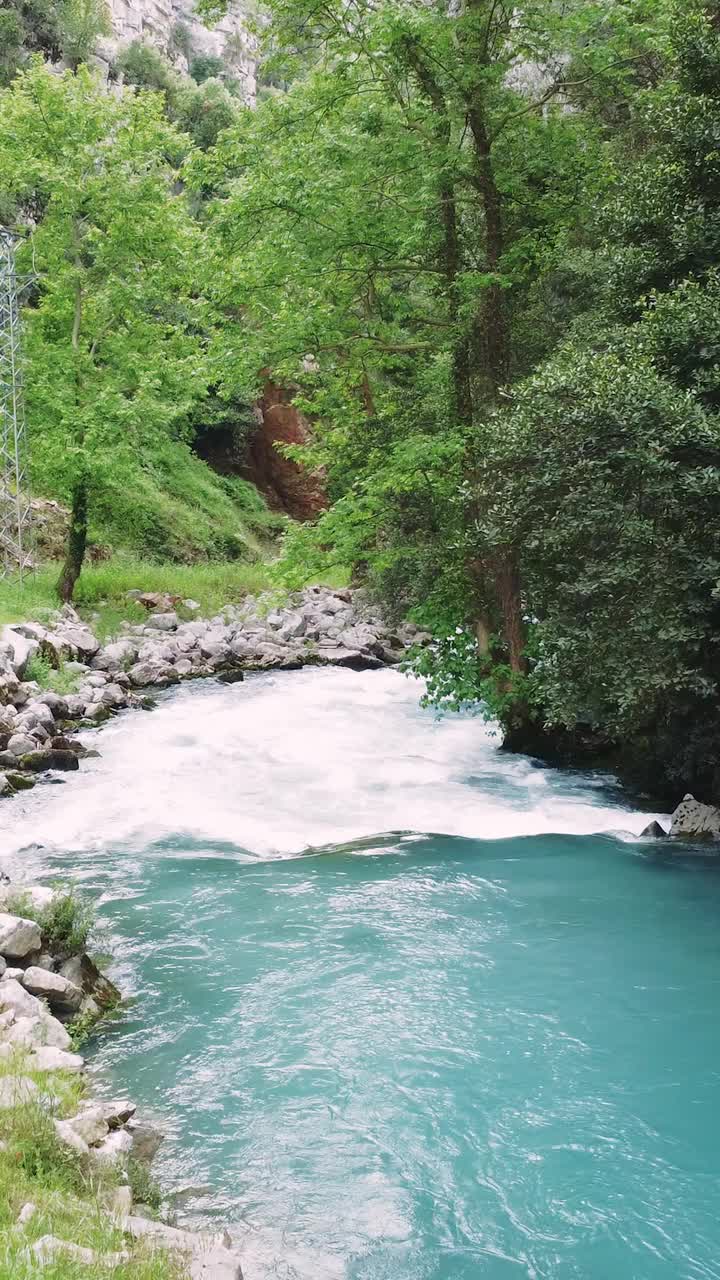 一架无人驾驶飞机在一条绿松石色的山间河流上低空飞行。山河流动迅速，显示其清澈的水。这段视频突出了山河在岩石地形中的动态运动视频素材