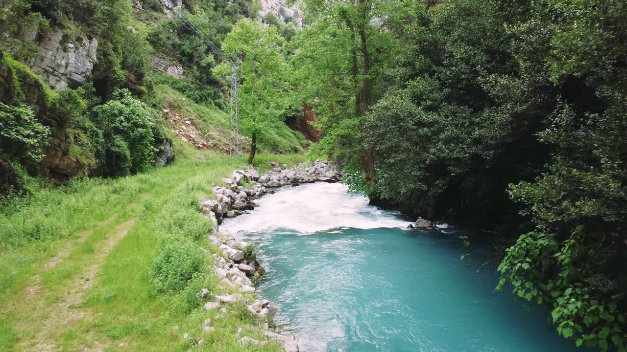 一架无人驾驶飞机在一条绿松石色的山间河流上低空飞行。山河流动迅速，显示其清澈的水。这段视频突出了山河在岩石地形中的动态运动视频素材