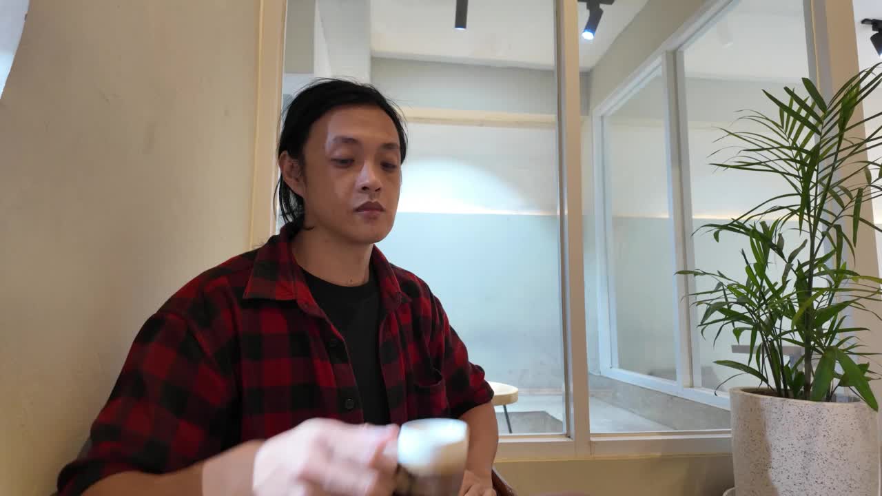 一个亚洲男人正在咖啡馆或咖啡店放松地享受着一杯咖啡。4k视频片段视频下载