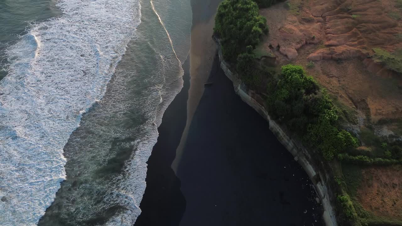 绿色的山丘和海浪拍打着黑色的沙滩视频素材