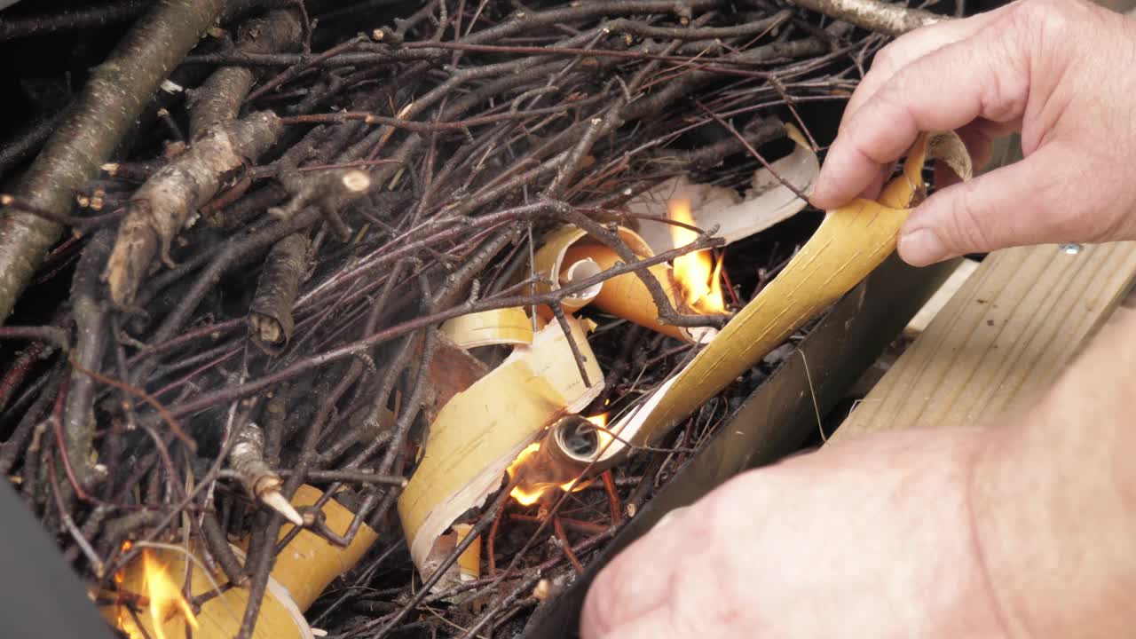 一个男人用干树枝和蔷薇树皮点燃火盆。视频下载