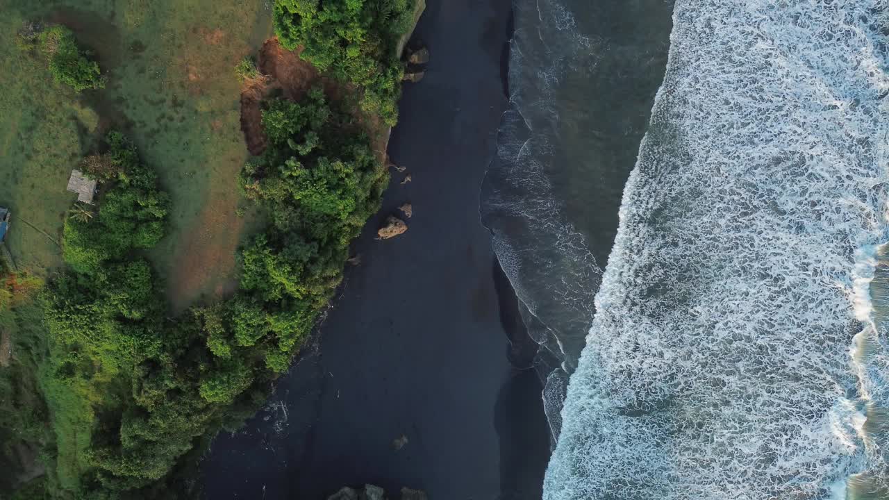 从空中俯瞰，绿色的山丘和巨大的海浪冲击着黑色的沙滩视频素材